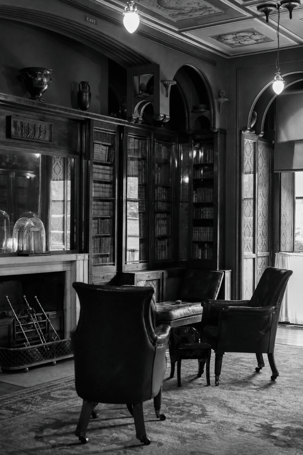 A period library with leather armchairs, glass-fronted bookcases and a fireplace, lit by pendant lamps